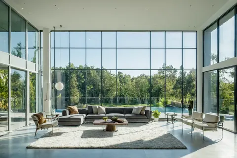A spacious modern living room with large windows overlooking a forest and pool.
