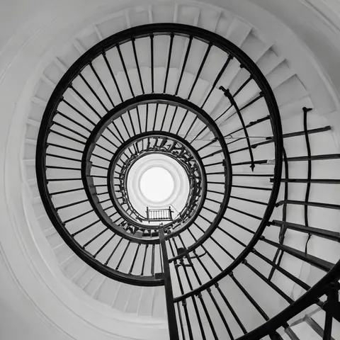 Black and white spiral staircase ascending toward a bright circular skylight