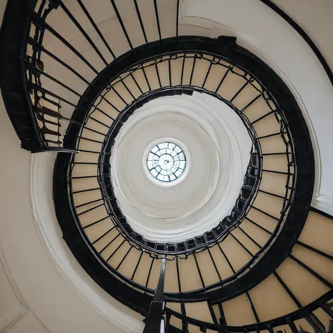 Black spiral staircase with wrought iron railings leading to a circular skylight in a cream dome ceiling.
