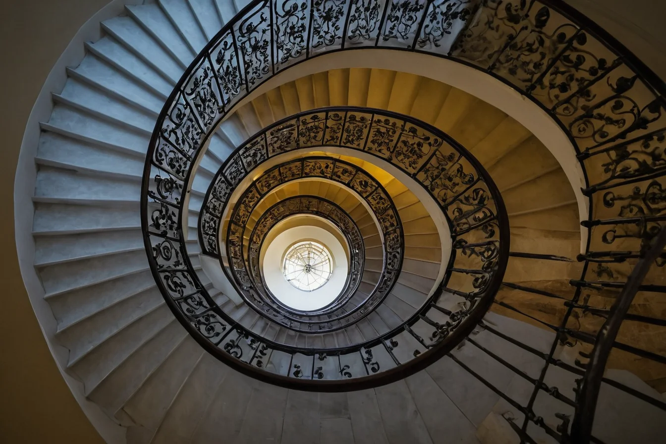 Grand spiral staircase with decorative iron railings leading to a skylight
