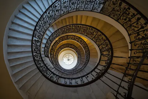 Grand spiral staircase with decorative iron railings leading to a skylight