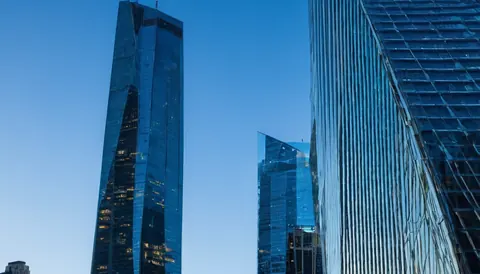 Modern glass skyscrapers reflecting blue sky and city lights at dusk