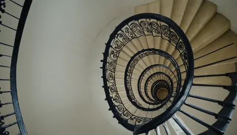 Spiral staircase with black iron railings and beige steps viewed from above
