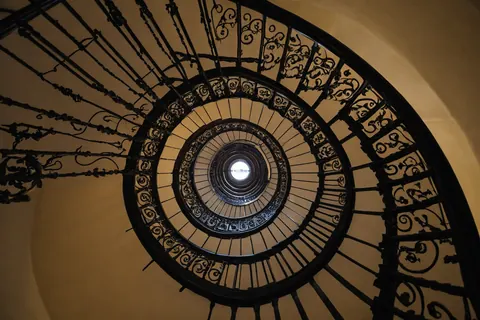 Spiral staircase with black iron railings and beige walls leading upward to a skylight
