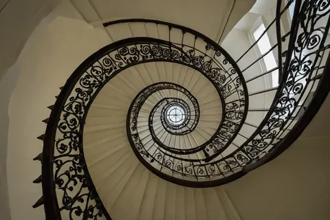 Spiral staircase with black iron railings and cream steps leading upward to a skylight.
