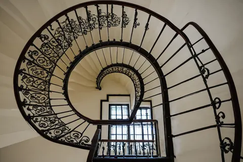 Spiral staircase with black iron railings and cream walls leading to a windowed landing