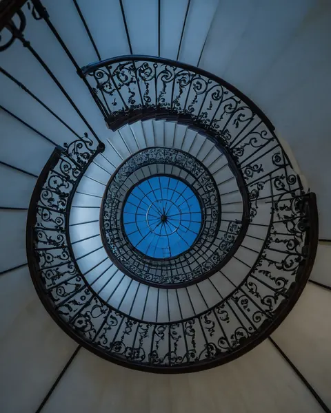 Spiral staircase with black iron railings leading to a blue skylight