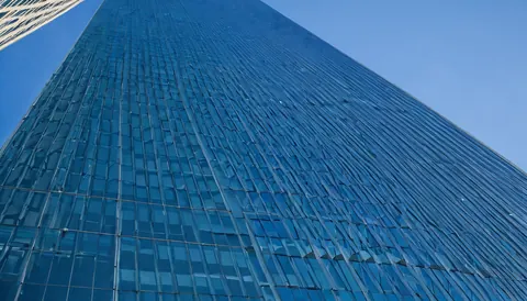 Towering blue glass skyscraper viewed from below against a clear sky