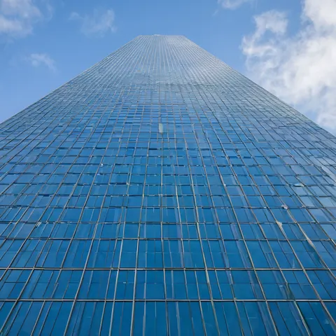 Towering glass skyscraper against a blue sky with white clouds