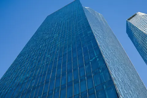 Towering glass skyscraper against a clear blue sky with another building nearby.