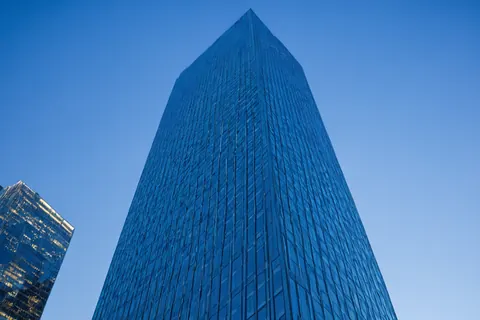 Towering glass skyscraper against clear blue sky with another building partially visible