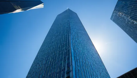 Towering glass skyscraper reaching into clear blue sky with sun glare