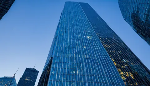 Towering glass skyscraper with glowing windows against a clear blue evening sky
