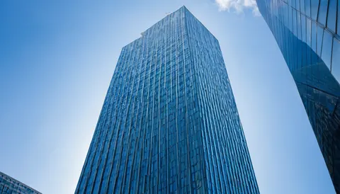 Towering glass skyscraper with reflective windows against a clear blue sky