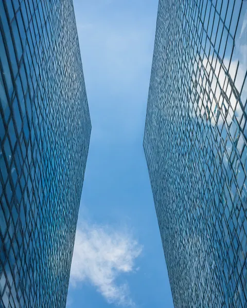 Two modern glass skyscrapers with diamond patterns frame a blue sky with white clouds.